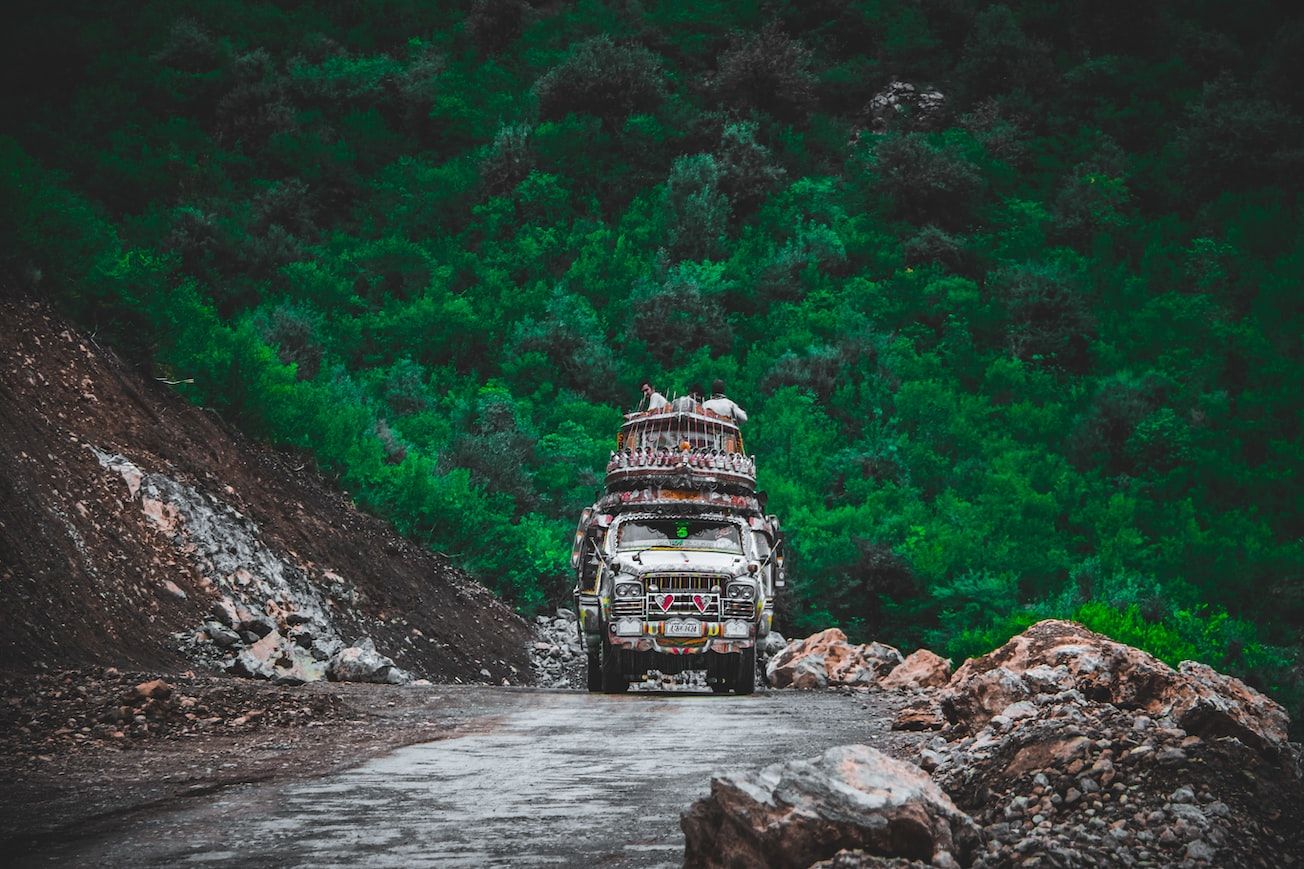 A colorful Pakistani truck grinds up a road through a forested hill