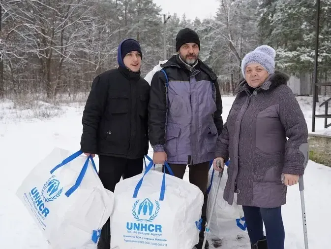Three villagers in Ukraine's Kyiv Oblast receive winter kits from UNHCR and local partner Right to Protection in 2023 so they can insulate their damaged home.