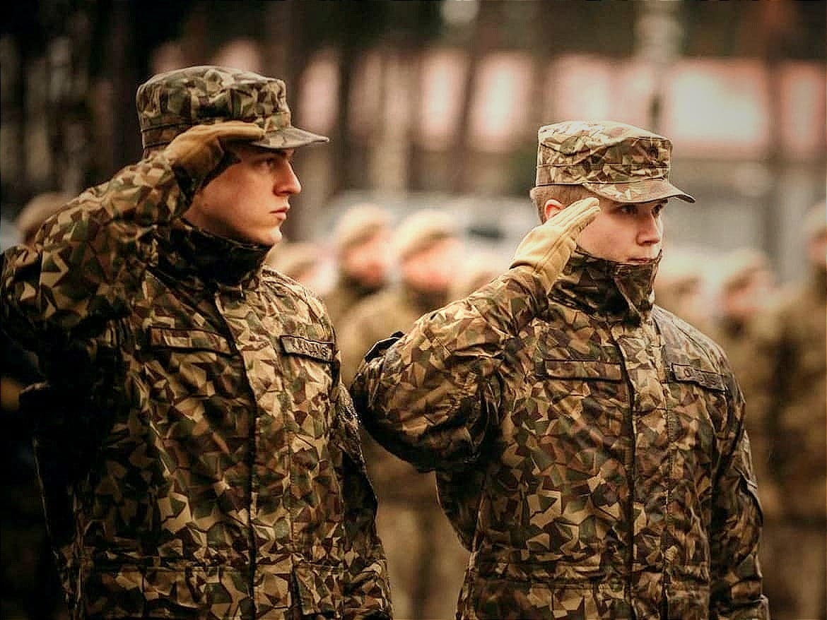 Krišhānis Kaļāns, left, stands at salute at an April 2024 ceremony where he was awarded a letter of honor for promoting the National Defense Service's media visibility. 